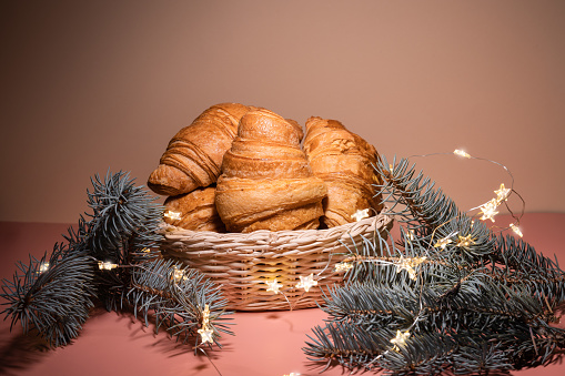 New Year's still life with fresh pastries. Croissants in a basket with spruce branches and lights. New Year's table setting, Christmas. Copy space banner