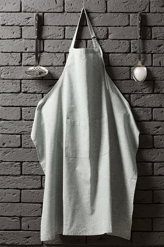 Clean apron with pattern and kitchen tools on grey brick wall