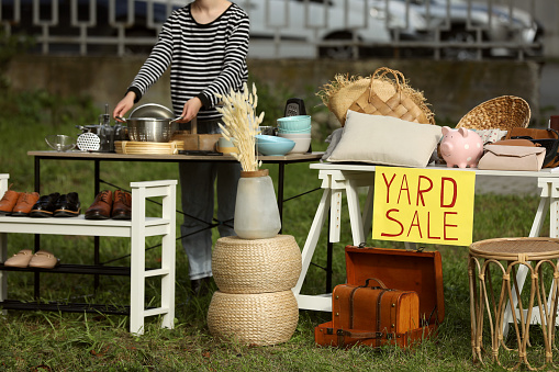 Woman near tables with different stuff on garage sale outdoors
