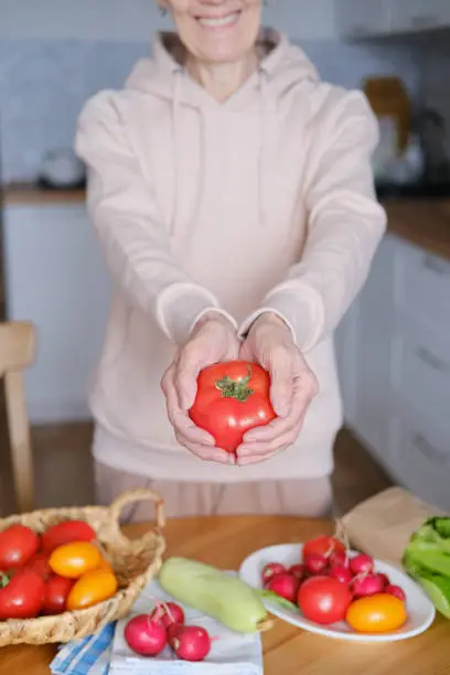 Photo of Age woman holding a large ripe tomato in her hands