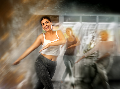 Group of positive women who care about their physical health practice active dancing during a workout in a fitness studio