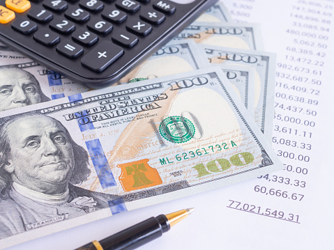 Business and financial concept. Money background, stack of 100 us dollar bills and list of financial figures, calculator on workplace. Close-up, Profit, savings, finance and wealth.