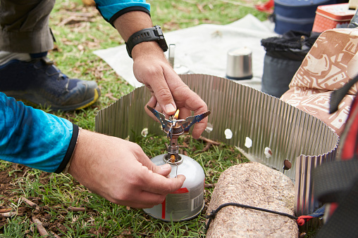 Unrecognizable man lighting a camp stove to cook at a campsite. Concepts: backpacking travel, camping lifestyle.