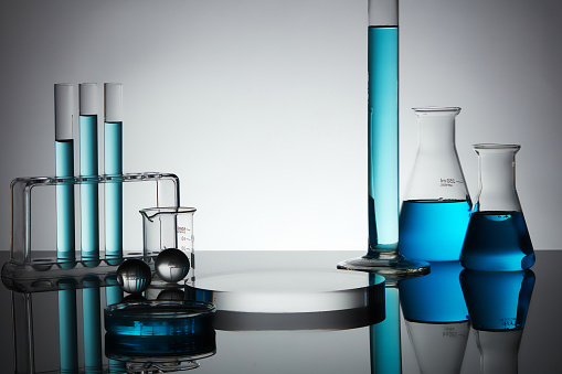 Blue liquid is filled inside petri dish and some laboratory glassware, decorated with glass balls and round podium. Blank space to display product