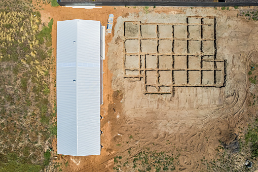 Aerial view looking directly down on house construction site: excavated waffle beams for reinforced concrete slab next to newly completed shed. Distinctive mostly square patterns in excavated foundation channels ready for adding reinforcing prior to pouring concrete slab.