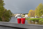 Disposable paper cup with coffee on the railing of bridge against the blurred background of moorage on the river.