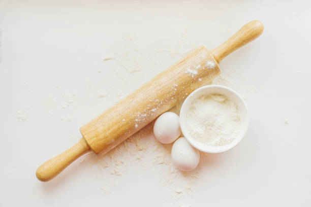 Rolling pin, eggs and a bowl with flour on a white table.