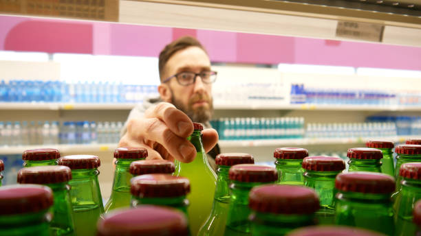 Close-up of many green glass bottles of sweet soda  or juice on a supermarket shelf and a male buyer takes two stock photo