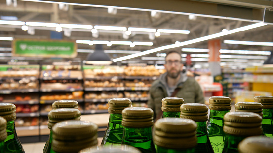 Many green glass bottles of mineral water on a atore shelf close-up and a man standing behind them