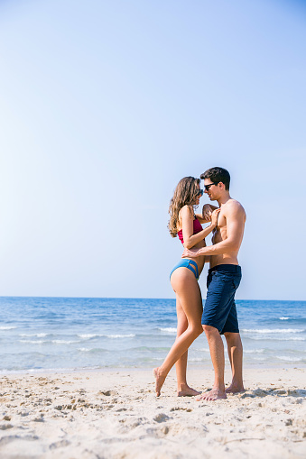 Portrait of beautiful couple of caucasian woman with man wearing sunglasses swim suit walk on beach. Young couple enjoy honeymoon after marriage at sea. Happy casual lover hold at tropical beach.