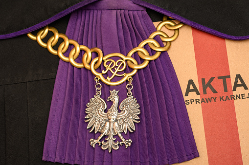 Judge's dress in Poland.  Black gown with purple elements.  On it is a chain and a court file with the inscription \