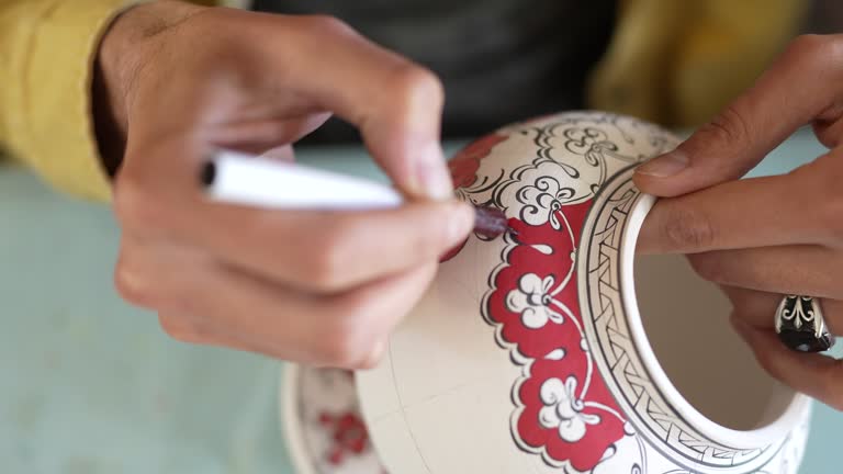 Man painting floral details on a vase in a ceramics studio