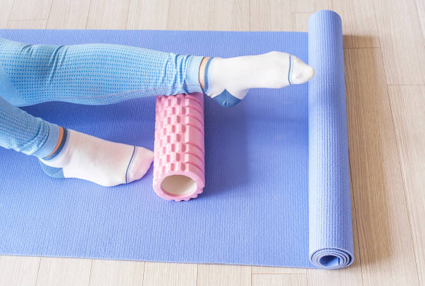 istock Female leg rolls a massage foam roller close-up on blue background. 1488283990