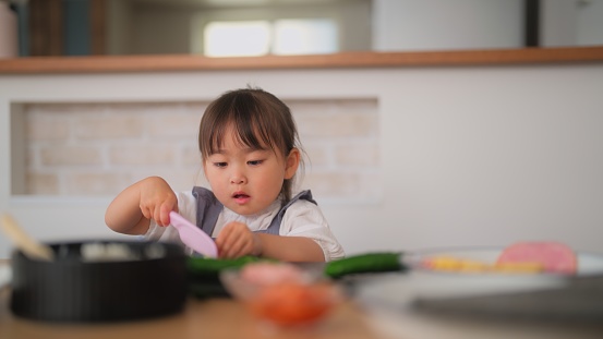 A small girl is cutting salad to make sushi together with her mother.