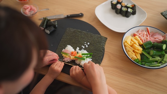 Detail of hands of woman chef rolling up japanese sushi with rice, avocado and prawns on nori seaweed sheet
