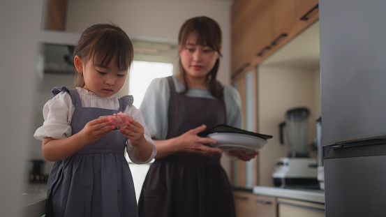 A mother is carrying sushi ingredients from kitchen with her small daughter.