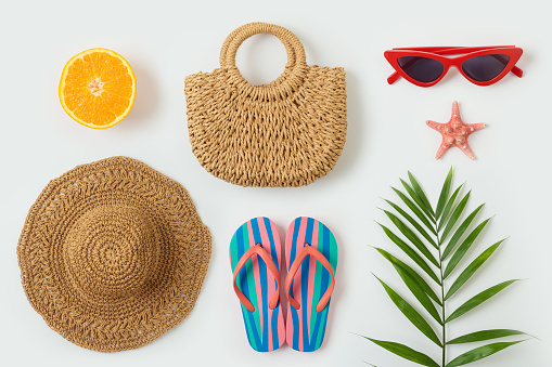 Summer vacation objects. Fashion bag; beach hat, flip flops and plam tree leaf  on white background. Top view from above