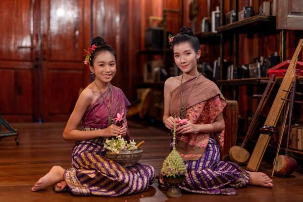 Asian women in traditional laos costume Portrait of two young and beautiful asian women wearing traditional Laos costume in a vintage old home. Preparing flowers for Loy Krathong festival celebration. traditional thai costume stock pictures, royalty-free photos & images