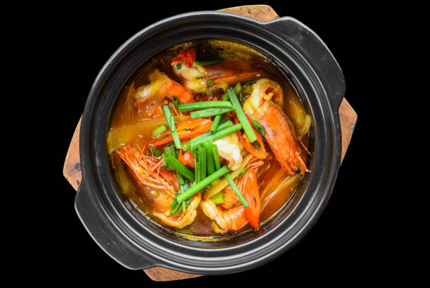 Shrimps with vegetables in bouillon isolated on black background top view