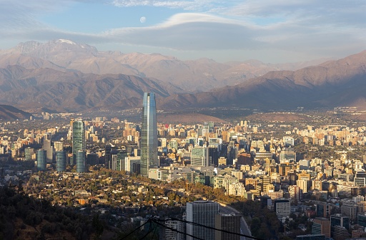 Panoramic View from Cerro Cristobal Hill with Famous Costanera Tower on City Downtown Skyline. Full Moon Rising over Distant Andes Mountains in the Background