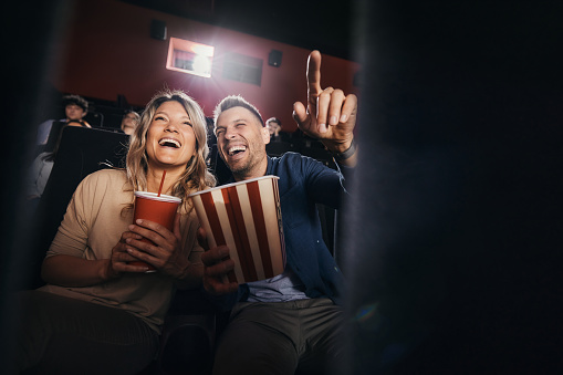 Happy couple having fun while watching a funny movie in cinema. Man is aiming at something. Copy space.