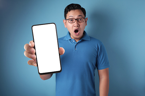 Young Asian man looking to camera, smiling and showing empty blank white copy space phone mock up template