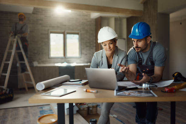 istock Female inspector and manual worker using laptop at renovating house. 1488301891
