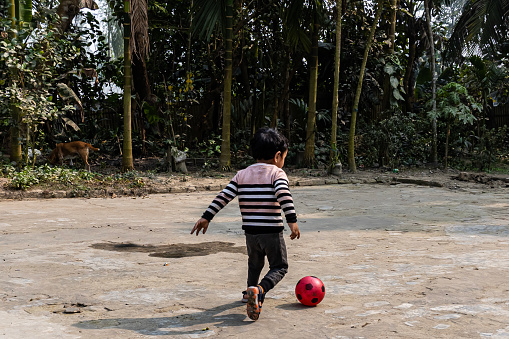 Boy kicking football on the house yard. Boy Running After Black and Red Soccer Ball. Kid Children Playing Football Fun Happiness Concept.