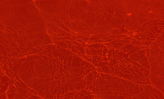 Redwater with ripples on the surface. Defocus blurred transparent red colored clear calm water surface texture with splashes and bubbles. Water waves with shining pattern texture background.