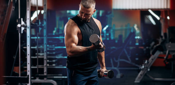 istock Muscular man doing biceps workouts with dumbbells in gym, copy space 1488307326