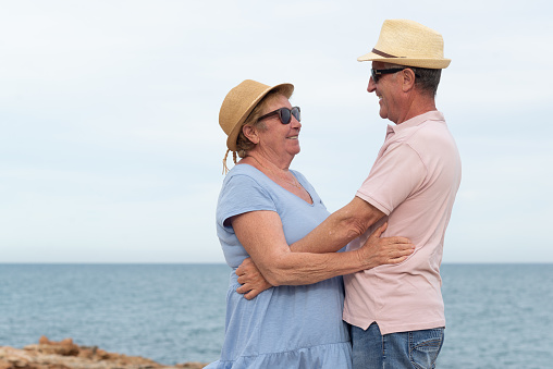 Profile view of a smiling senior couple embracing and looking each other with the sea on the background.