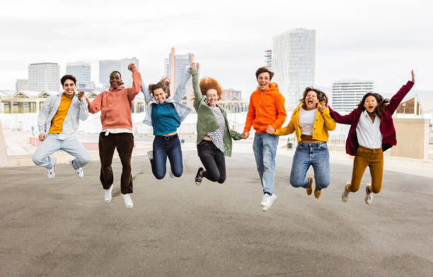 Diverse happy group of young friends jumping together outdoors stock photo