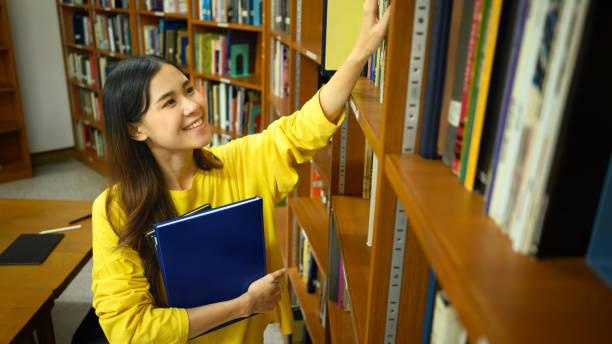 istock Cheerful Asian female student taking book from shelf in library. Education, knowledge and people concept. 1488309358