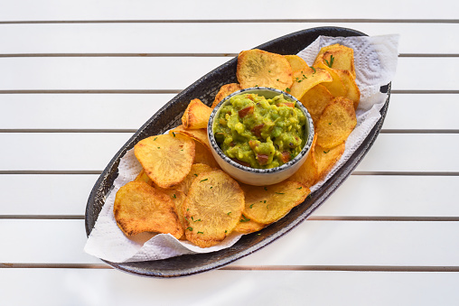 Homemade potato chips with vegetarian sauce made of avocado and vegetables on white wooden table