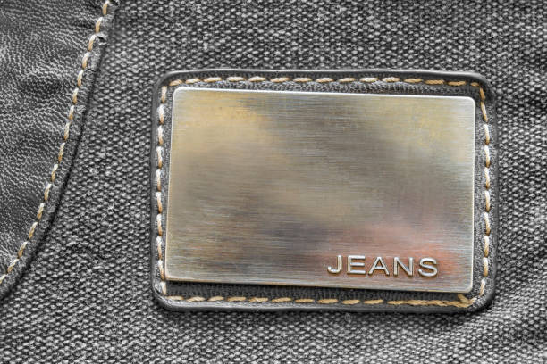 Metal plate says jeans stitched on grey fabric background