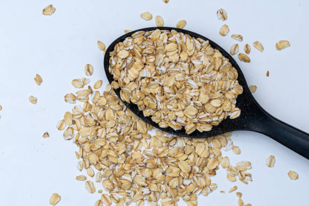 istock Oat flakes scattered on a black kitchen spoon on a white background 1488313889