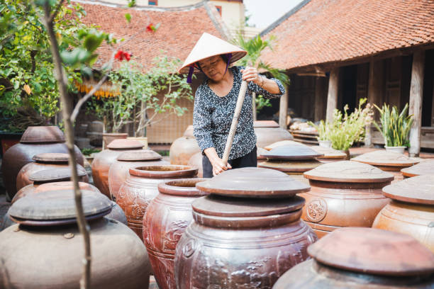 vietnamese senior woman stirring in huge clay soy pod in courtyard - asian cuisine food asian ethnicity vietnamese cuisine imagens e fotografias de stock