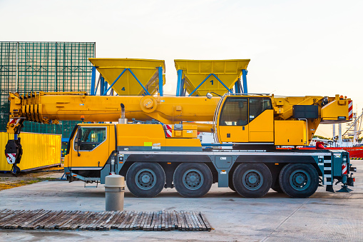 A yellow wheeled truck crane stands in the port. Heavy wheeled loading equipment.