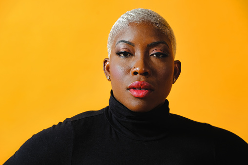 Portrait of mid adult black woman with short bleached hair wearing black turtleneck against yellow studio background