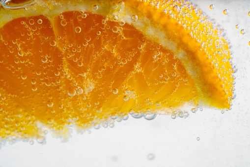 A closeup shot of an orange slice suspended in water and surrounded by bubbles on a white background.