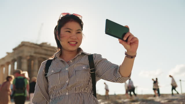 Greece, Athens, Asian woman traveller taking a cell phone picture of the ruin temple in the Acropolis daytime travel concept