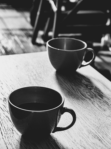 black and white shot against the light of the window. focus on the coffee cups, background in blur