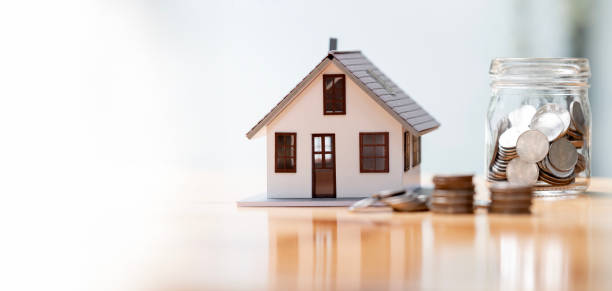 istock Real estate concept background. House model and coins stack on wooden table, copy space. 1488327115