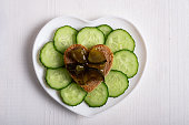 On a heart-shaped plate there is a cucumber cut into circles and heart-shaped bread with cucumber jam.