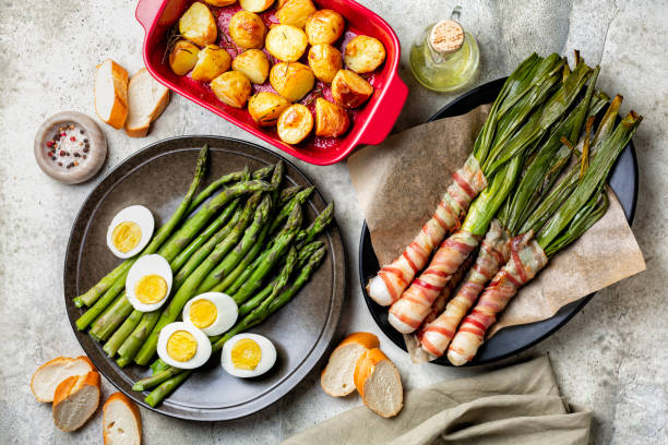Spring dish green asparagus with hard boiled eggs, sicilian bacon wrapped scallions or spring onions, baked in oven, oven-roasted new potatoes. Homemade simple food concept. Top view.