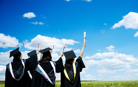 Rear view of four graduates holding diplomas