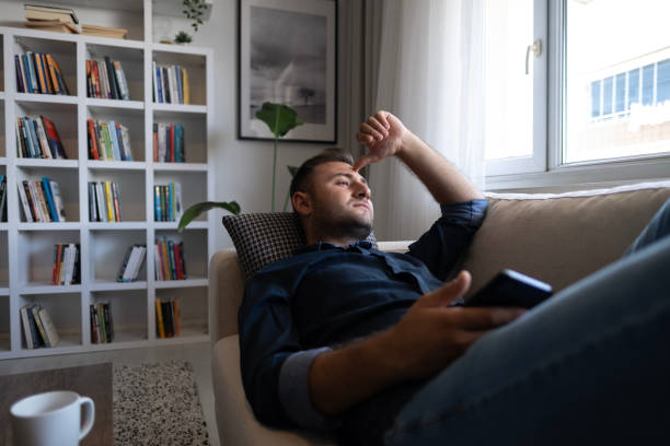 Thoughtful serious man sitting on sofa at home, lost in thoughts