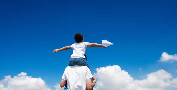Son sitting father's shoulder and throwing paper plane