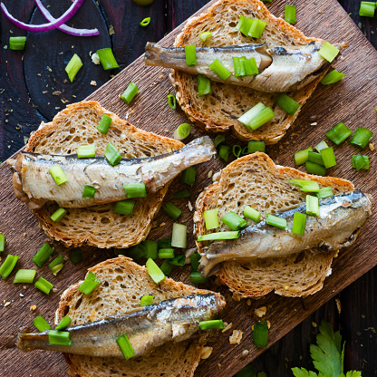 sandwich with sardines, sprinkle with onions on a cutting board on a black background with fennel and red onion