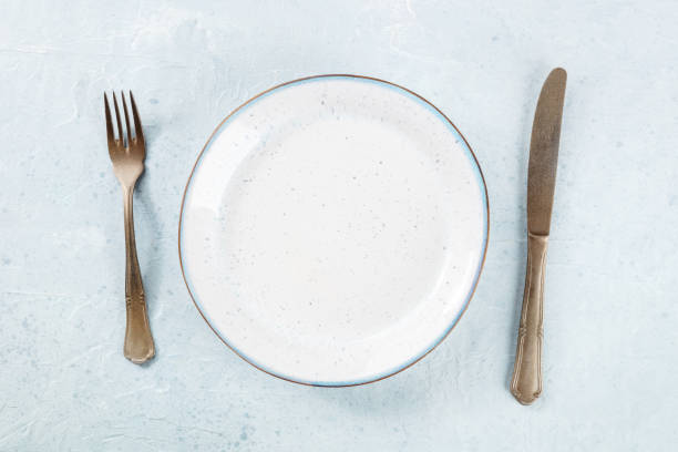 istock An empty white plate with a blue rim, with a fork and a knife, overhead 1488333512